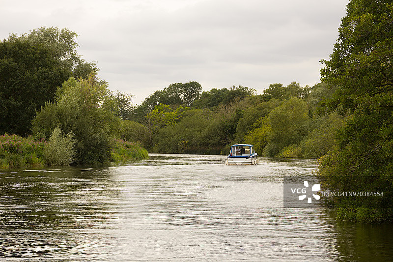 在英国萨福克郡的布罗ads国家公园中蜿蜒的韦弗尼河上缓慢行驶的河船，驶往贝克尔斯镇图片素材
