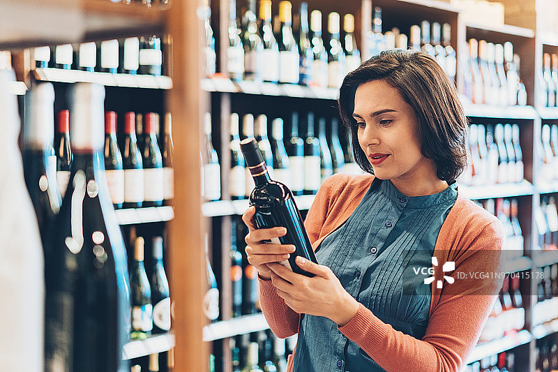 年轻女人在葡萄酒商店手拿酒瓶图片素材