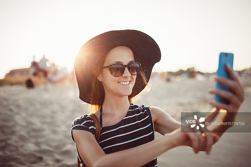 微笑的女人在日落时分的沙滩上自拍图片素材