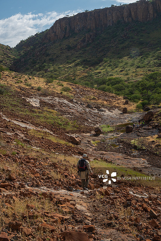 年长登山者沿着蜿蜒的小路穿过岩石走向她在纳米比亚埃滕代卡山上的同伴（模特已授权）图片素材