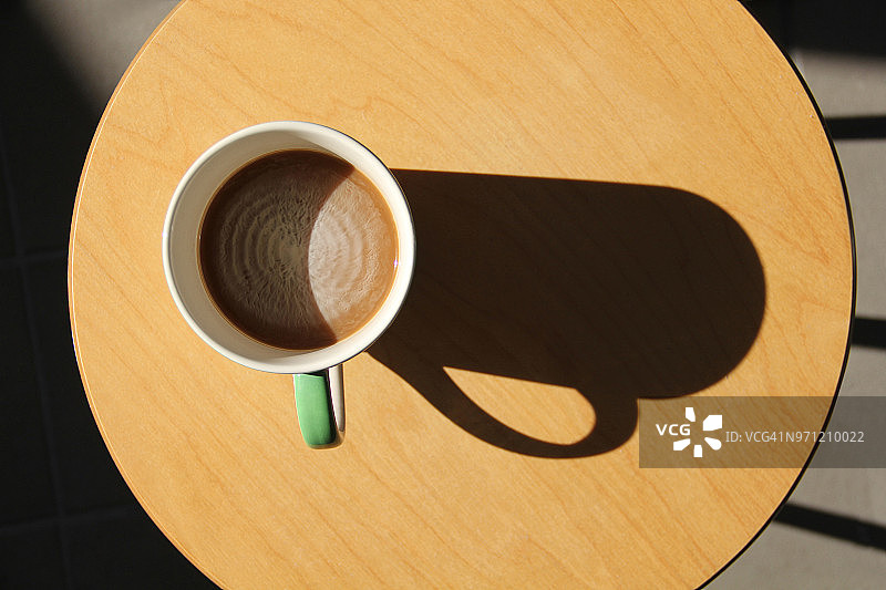 木桌上带大阴影的咖啡杯特写图片素材