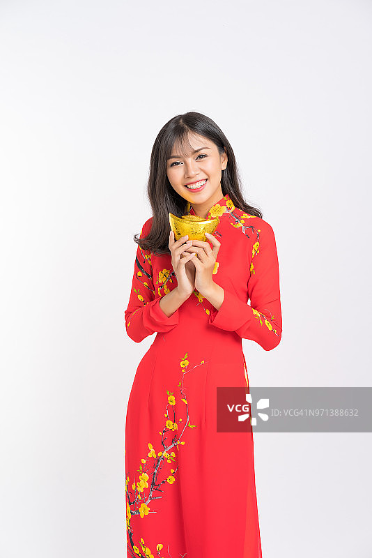 年轻女人身穿越南红色奥黛，微笑地抱着一堆新年金元宝图片素材