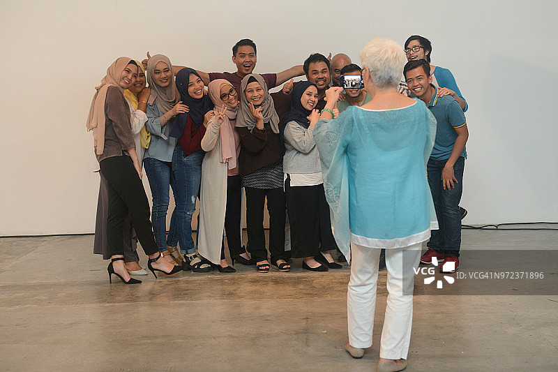 快乐的老年妇女和年轻的朋友在工作室聚会，用手机自拍图片素材