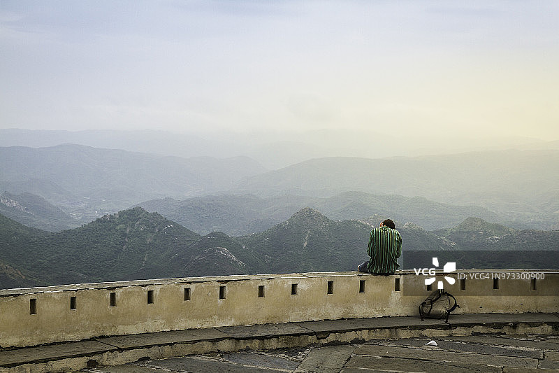 徒步旅行者坐在墙上，眺望印度拉贾斯坦邦乌代浦尔的群山图片素材