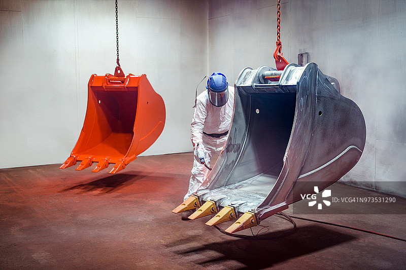 喷漆工在工程工厂的喷漆室中喷涂挖掘机铲斗图片素材