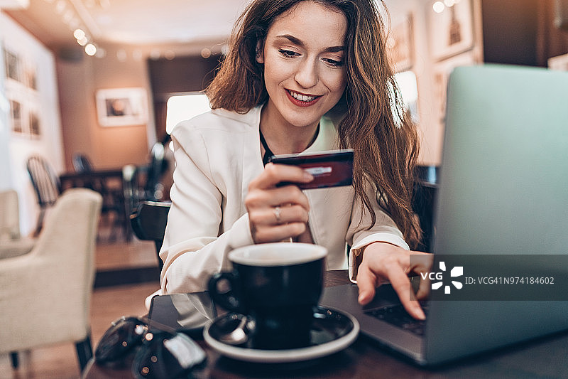 年轻女子在咖啡馆使用笔记本电脑和信用卡图片素材