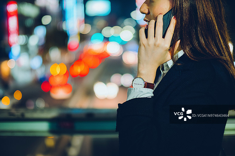 亚洲女商人夜晚在繁忙的城市街道上打电话等出租车图片素材
