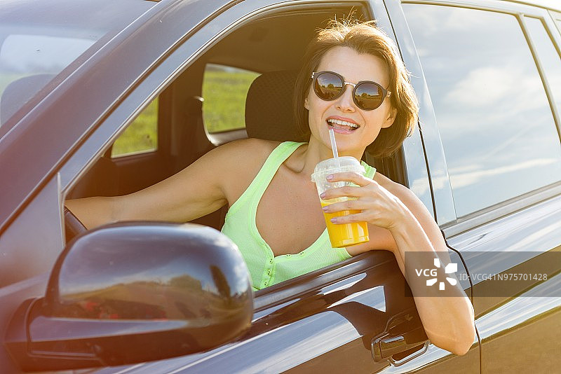 快乐的女司机对你微笑，停下来放松，享受旅程，喝橙汁图片素材