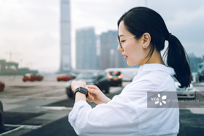 年轻女人在城市户外停车场使用智能手表走向她的汽车图片素材