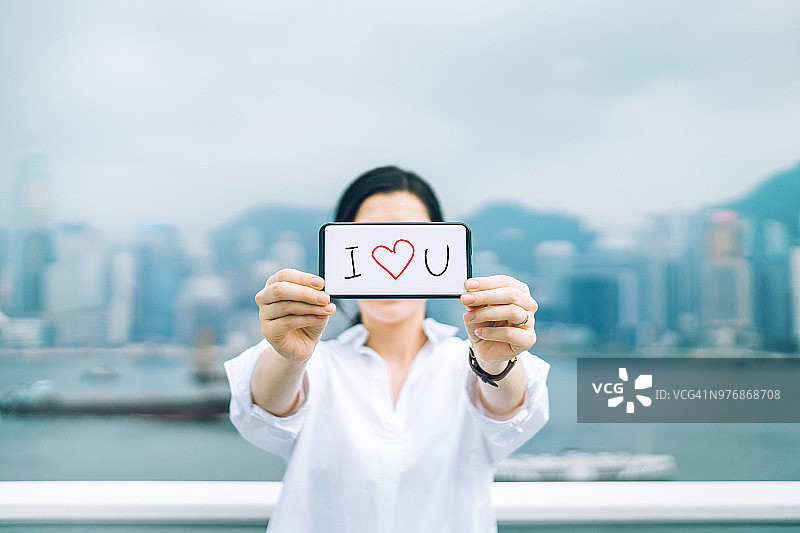 女人在城市天际线下用手机说“我爱你”图片素材