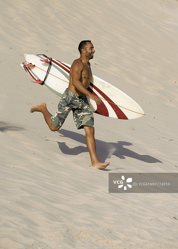 男人在海滩上跑步，手里拿着冲浪板图片素材