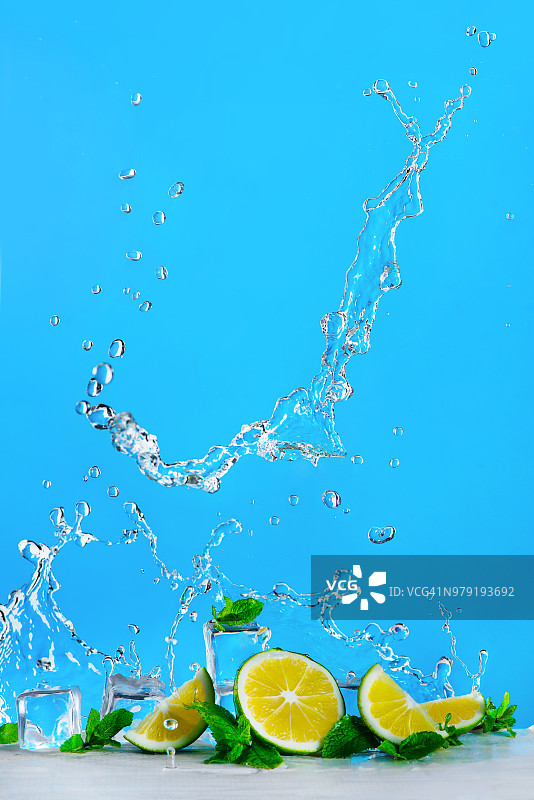 明亮蓝色背景上的青柠片、冰块、薄荷叶以及莫吉托或柠檬水的动态水花，清爽的夏季饮品概念，带有复制空间图片素材