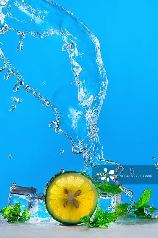 明亮蓝色背景上的青柠片、冰块、薄荷叶以及莫吉托或柠檬水的动态水花，清爽的夏季饮品概念，带有复制空间图片素材