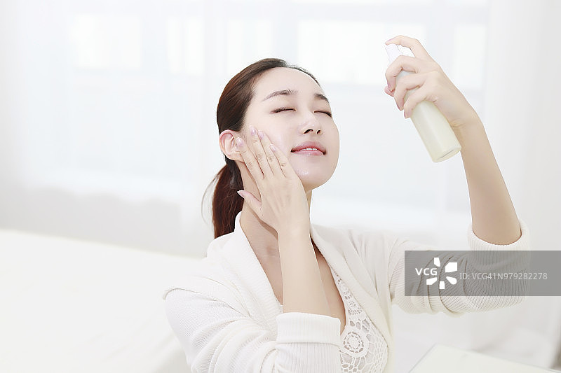 年轻女子闭着眼睛将水雾喷在脸上图片素材