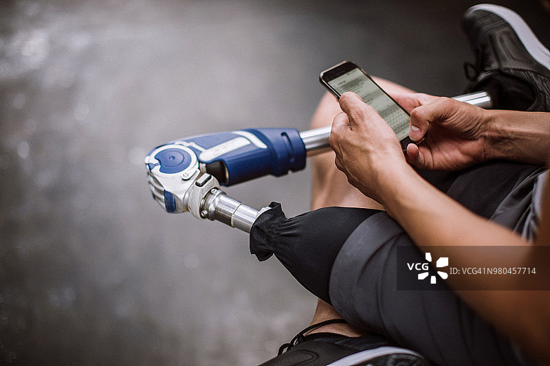 健身休息时使用手机的截肢男人图片素材