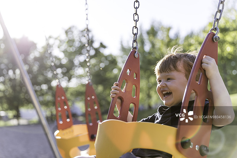 在户外游乐场秋千上快乐的红发幼儿男孩图片素材