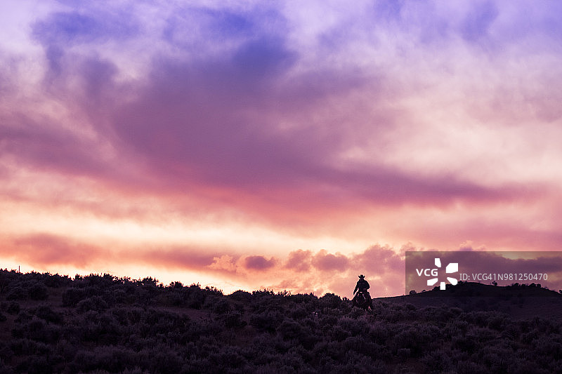 牛仔在日落时分骑马登山图片素材