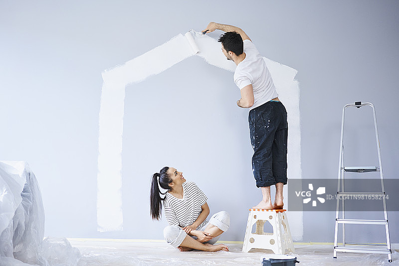 情侣在新公寓墙上绘制房屋图案图片素材
