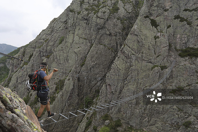 年轻男人沿着铁索攀岩路线攀登图片素材