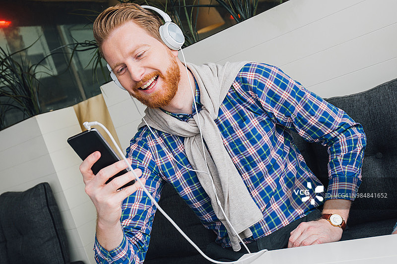 快乐的男人戴着耳机听音乐，看着手机图片素材