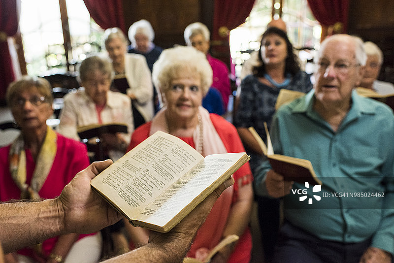 牧师手持赞美诗书，会众在背景中图片素材