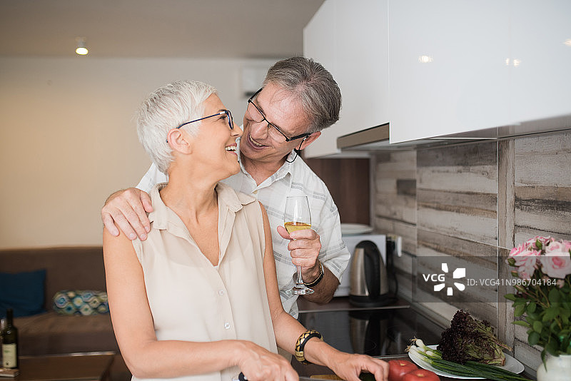 中年男人与妻子在厨房准备午餐，手持酒杯相拥图片素材