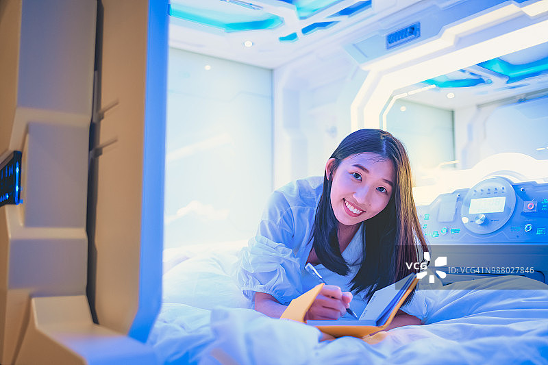 年轻的亚洲中国女人躺在胶囊旅馆的床上，对着镜头微笑图片素材