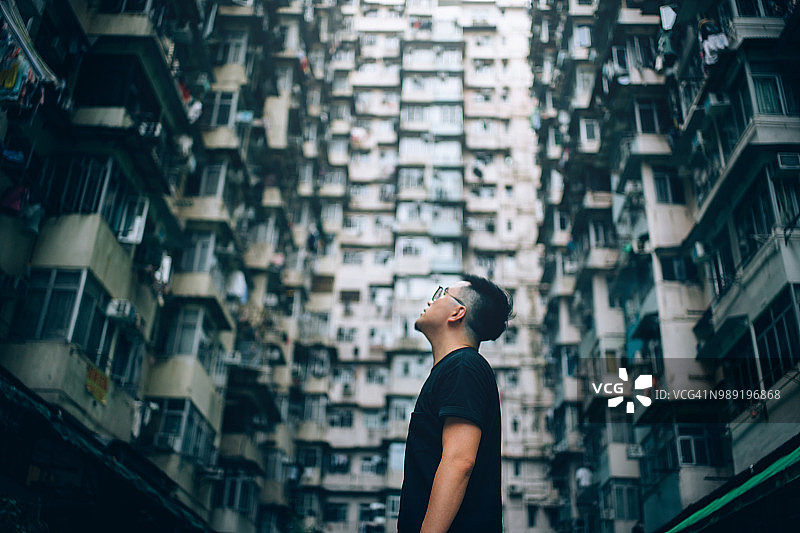 被旧式传统住宅建筑环绕，仰望城市天空的年轻男子的背影图片素材