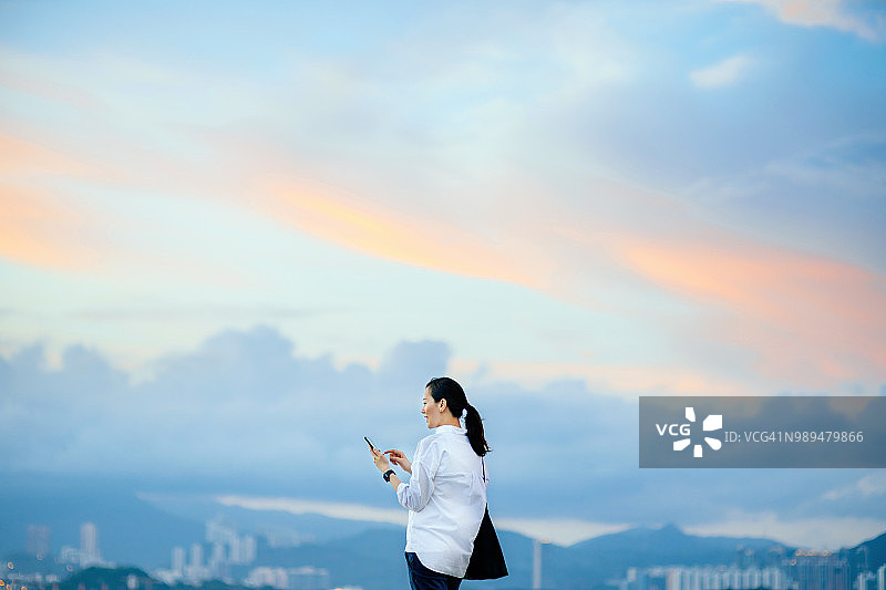 在城市天际线下使用智能手机的自信年轻女人图片素材