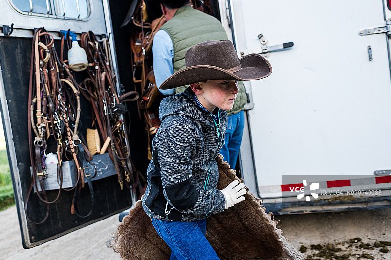 年轻牛仔从运马车上取下马具图片素材