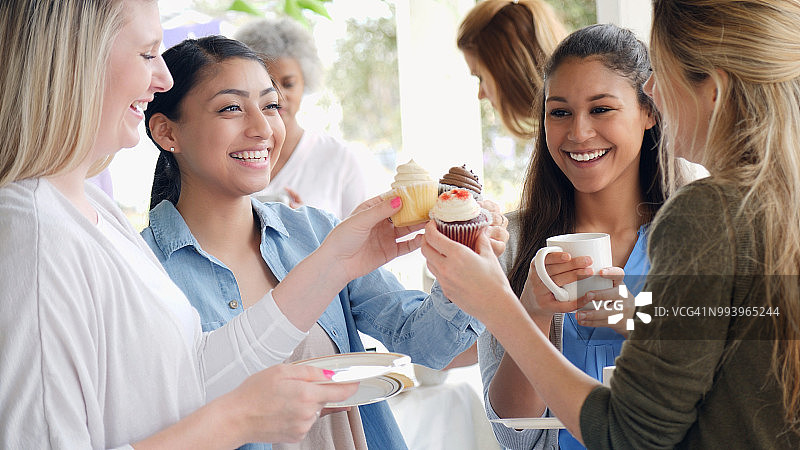 在慈善活动中，闺蜜们举着纸杯蛋糕开玩笑图片素材