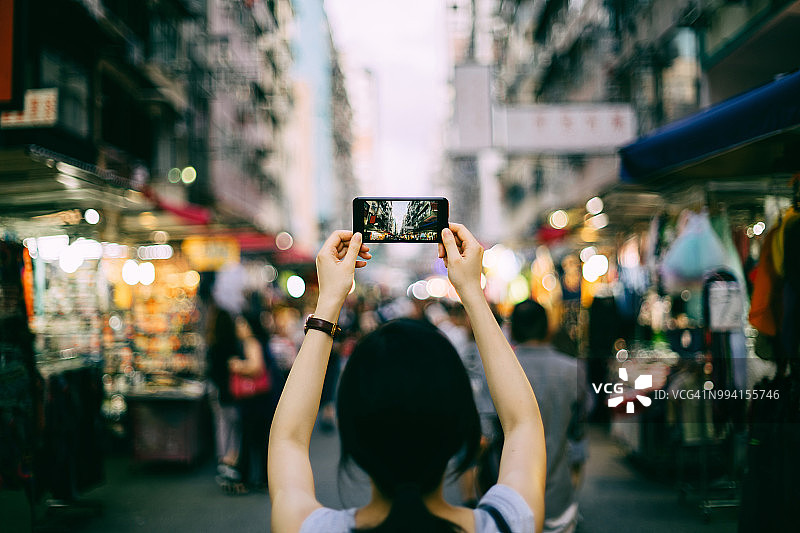 在香港当地街头市场探索时拍摄街景的女性旅行者背影图片素材