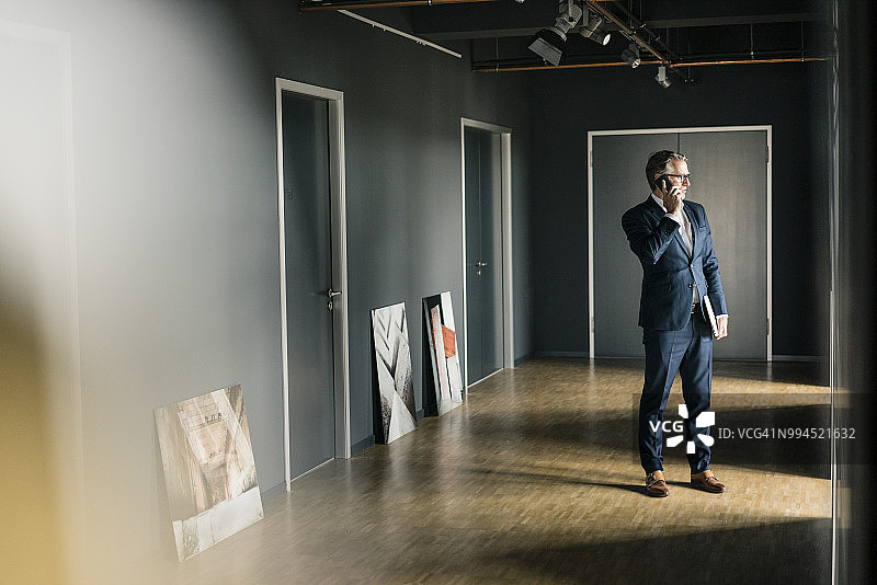 站在办公室地板上，一边看画一边使用手机的中年商人图片素材