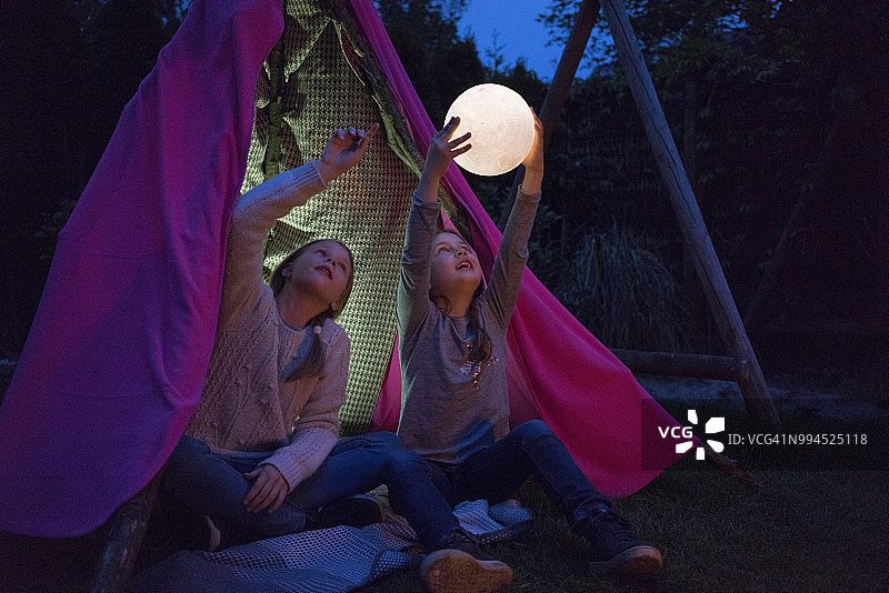 两个女孩坐在圆锥帐篷里，拿着灯当月亮图片素材