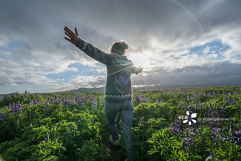 年轻女人在春日夕阳下的花田中伸展双臂，拥抱自由图片素材