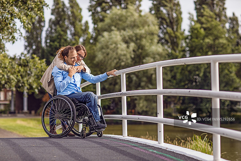 使用轮椅的年轻男子和女友在城市公园里散步图片素材