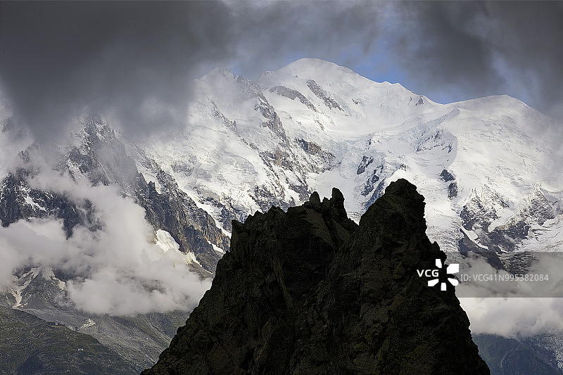 勃朗峰山块、沙莫尼山谷和勃朗峰顶峰的岩层轮廓，乌云密布和蓝色天空图片素材
