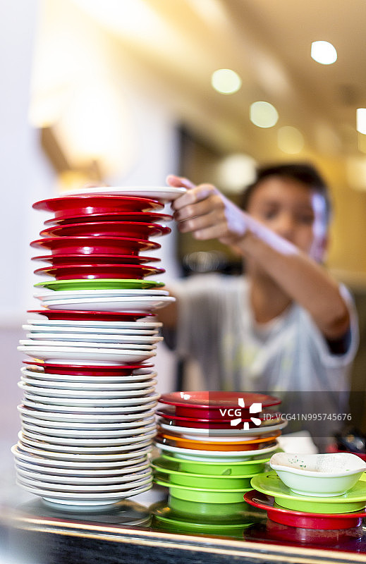 男孩在寿司店堆叠塑料盘图片素材