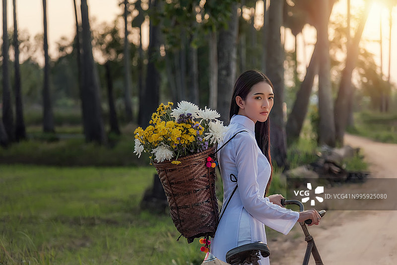 穿着越南奥黛的女人在村庄的道路上骑自行车图片素材