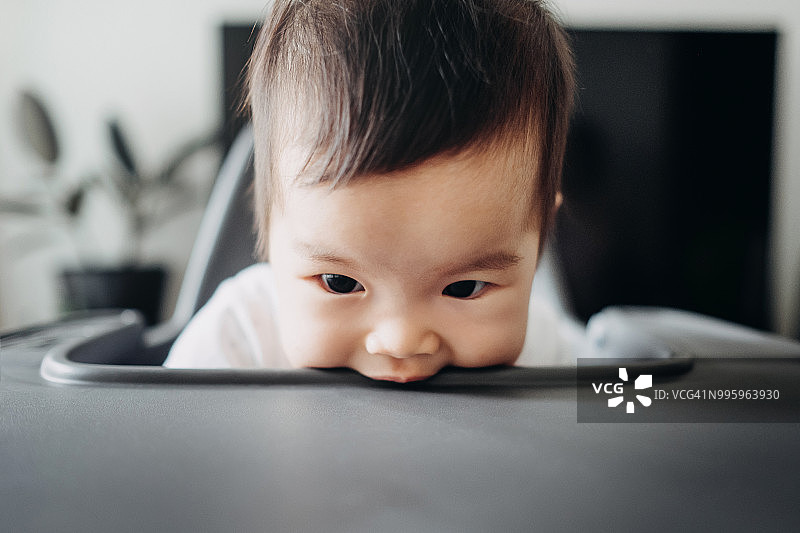 正在啃咬餐椅桌子的可爱宝宝图片素材