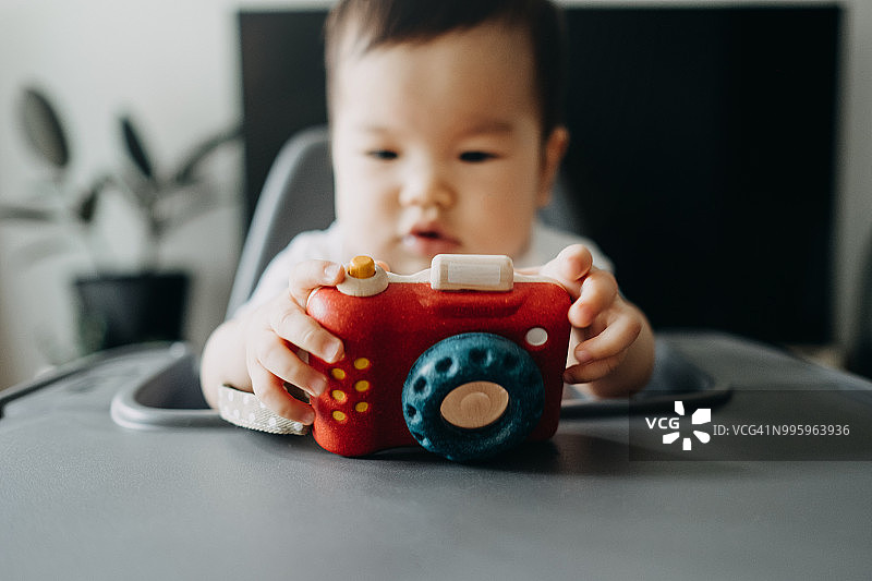 可爱宝宝在高脚椅上玩木制玩具相机图片素材