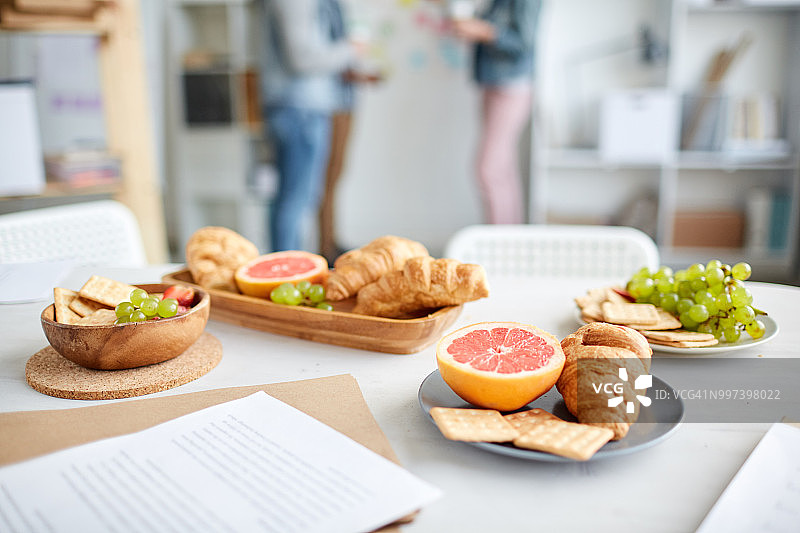 办公室休息时间与甜点：摆满水果、饼干和面包的办公桌特写图片素材
