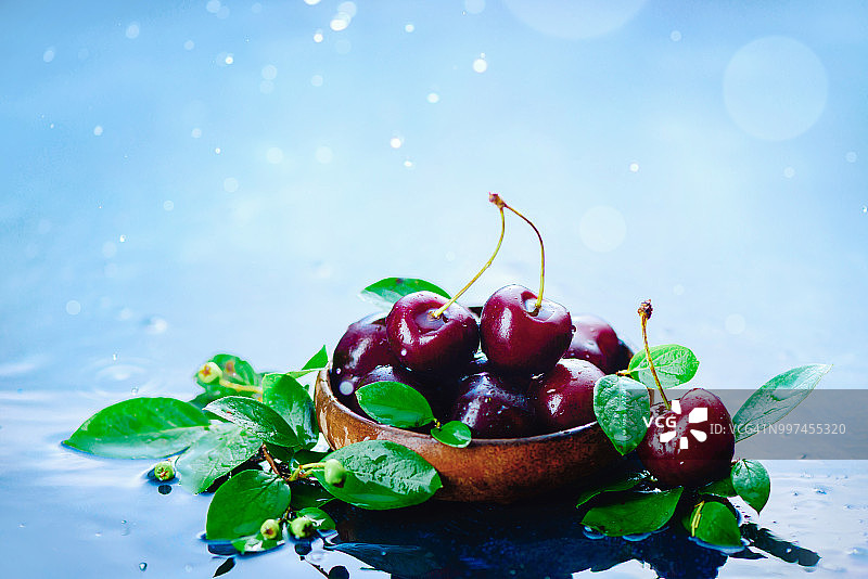 木碗中带有绿叶的成熟樱桃，浅色湿润背景，带有水滴。具有复制空间的收获概念。秋雨静物。图片素材