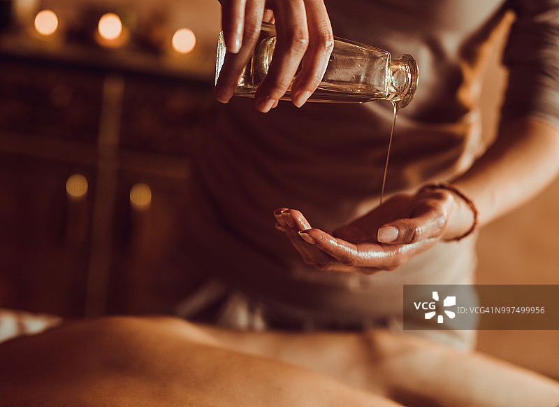 面部不可辨认的理疗师将按摩油倒入手图片素材