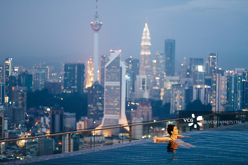 年轻女人在泳池放松，吉隆坡日落美景图片素材