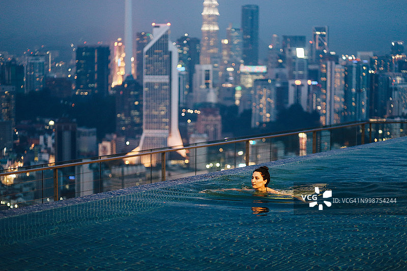 年轻女人在泳池放松，吉隆坡日落美景图片素材