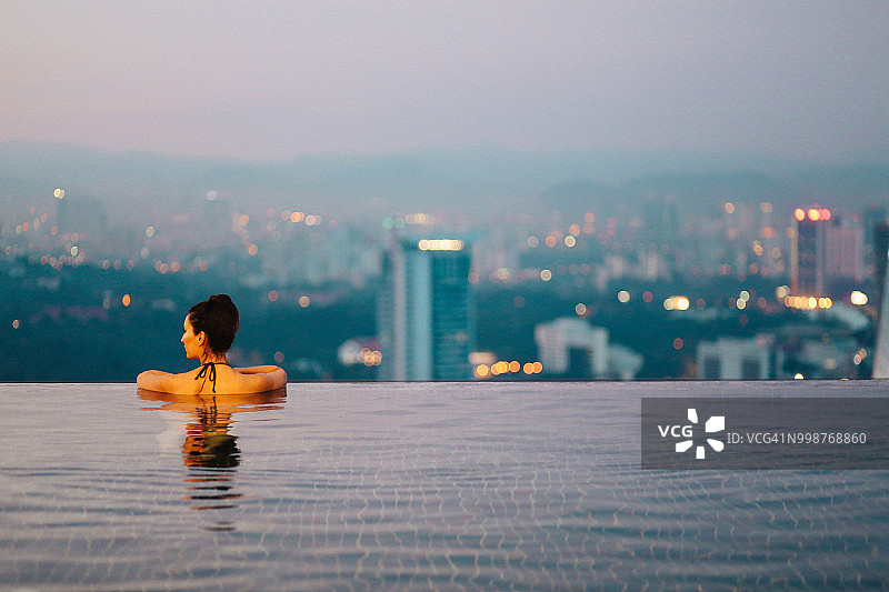 年轻女人在泳池放松，吉隆坡日落美景图片素材
