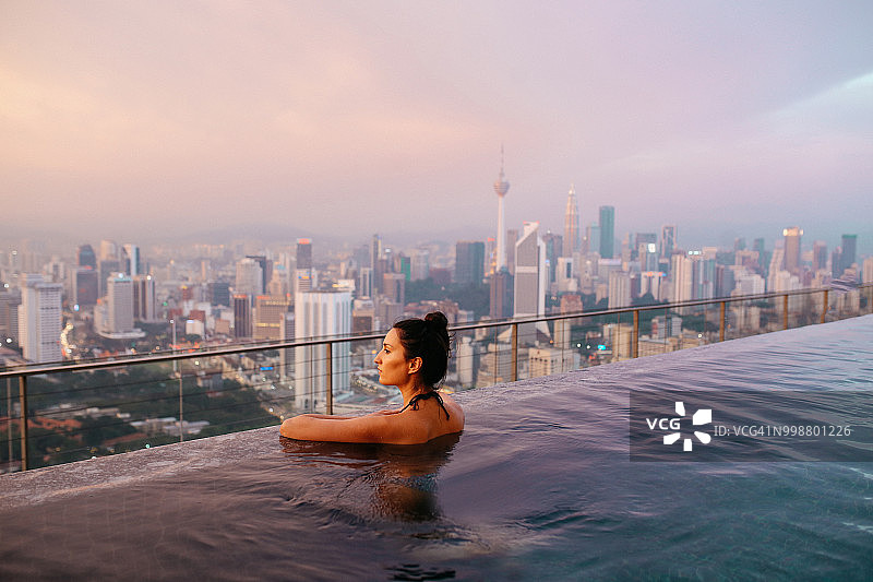 年轻棕发女子在泳池中放松身心，太阳在马来西亚吉隆坡上空落下图片素材