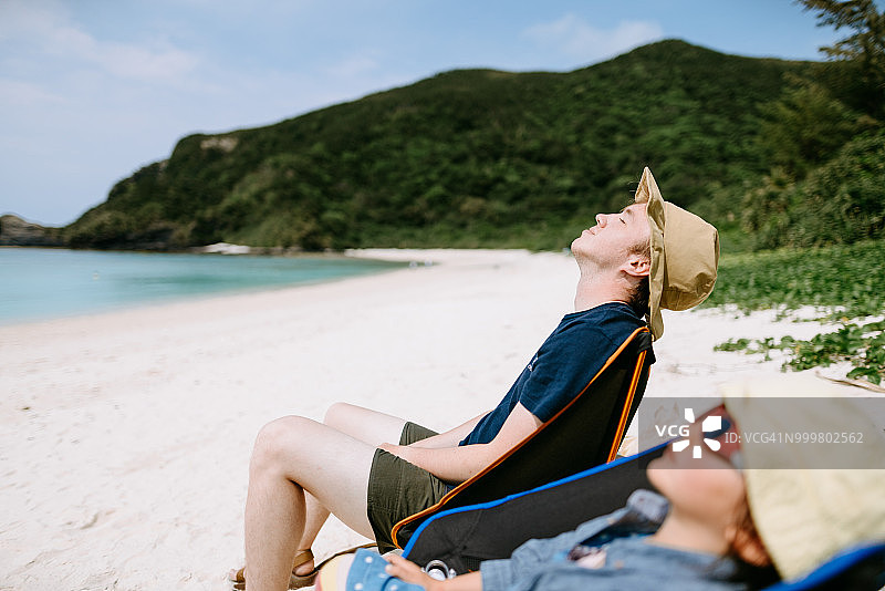 男人和孩子在冲绳热带海滩露营椅上放松图片素材