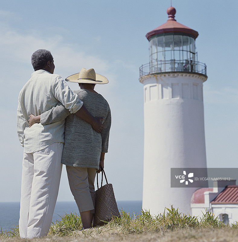中年夫妇手挽手站在灯塔前，后视图图片素材